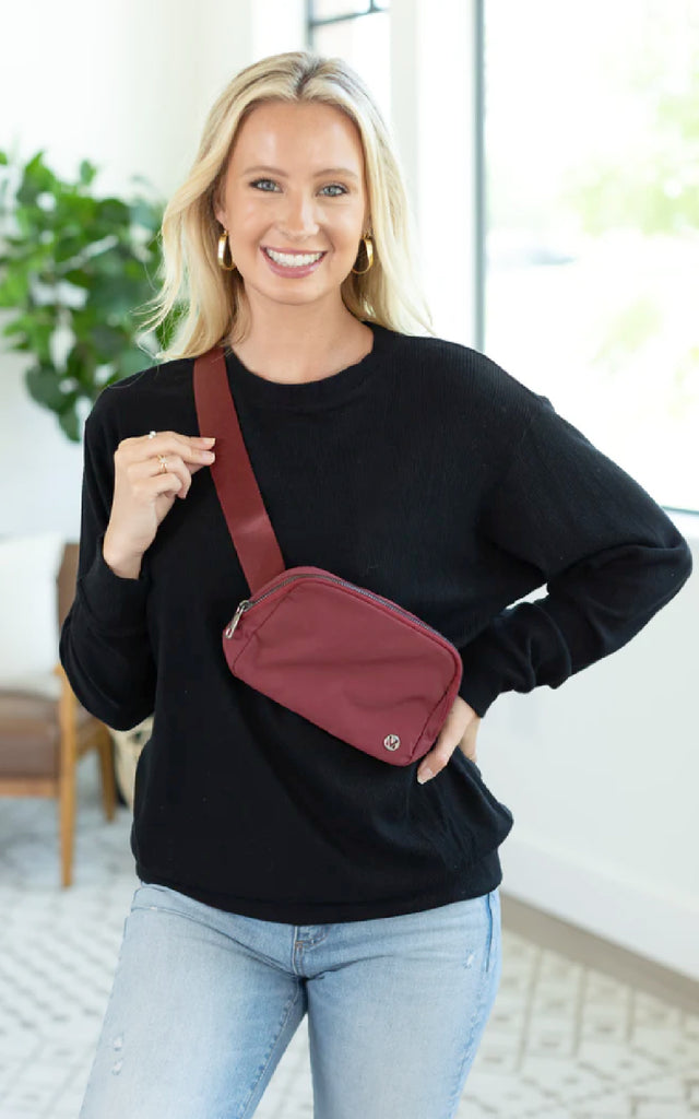 Woman wearing a wine colored bum bag across her chest.
