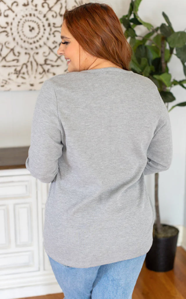 Woman wearing a long sleeve, light gray henley top.