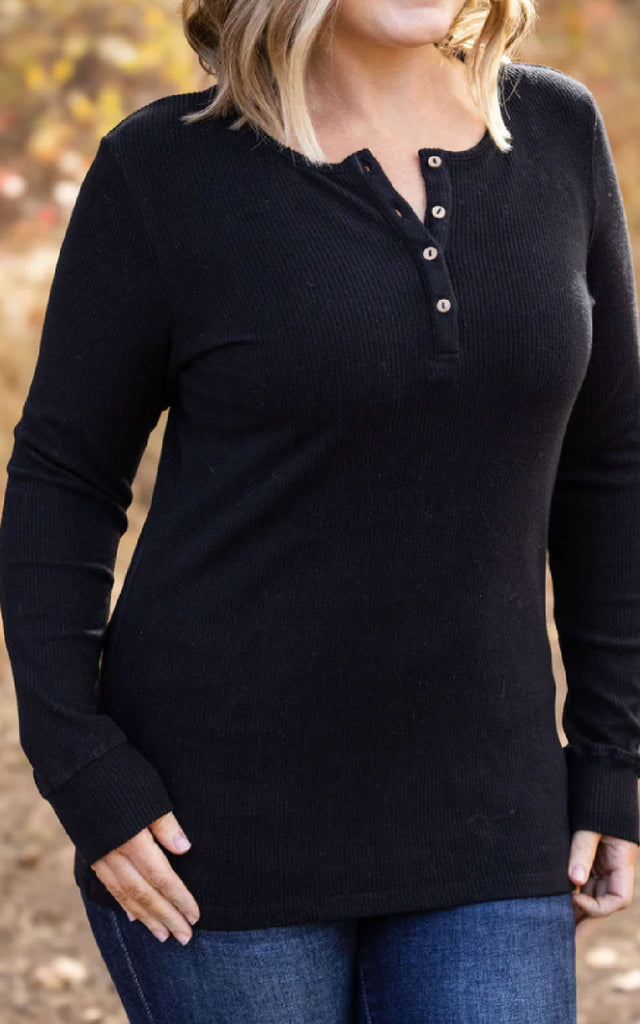 Woman posing while wearing a black henley long sleeve top.