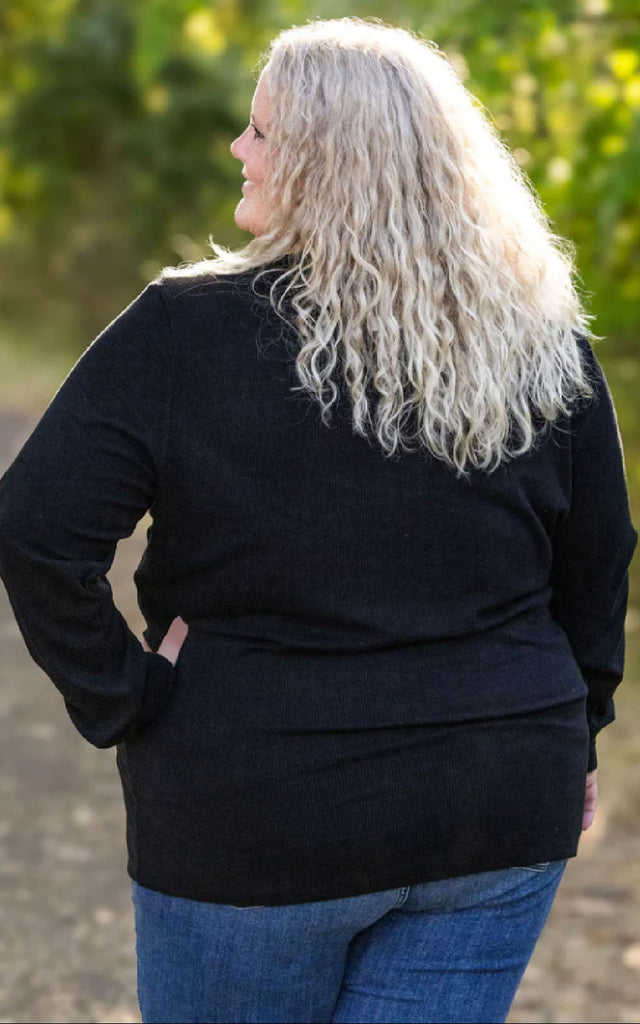 Woman posing while wearing a black henley long sleeve top.