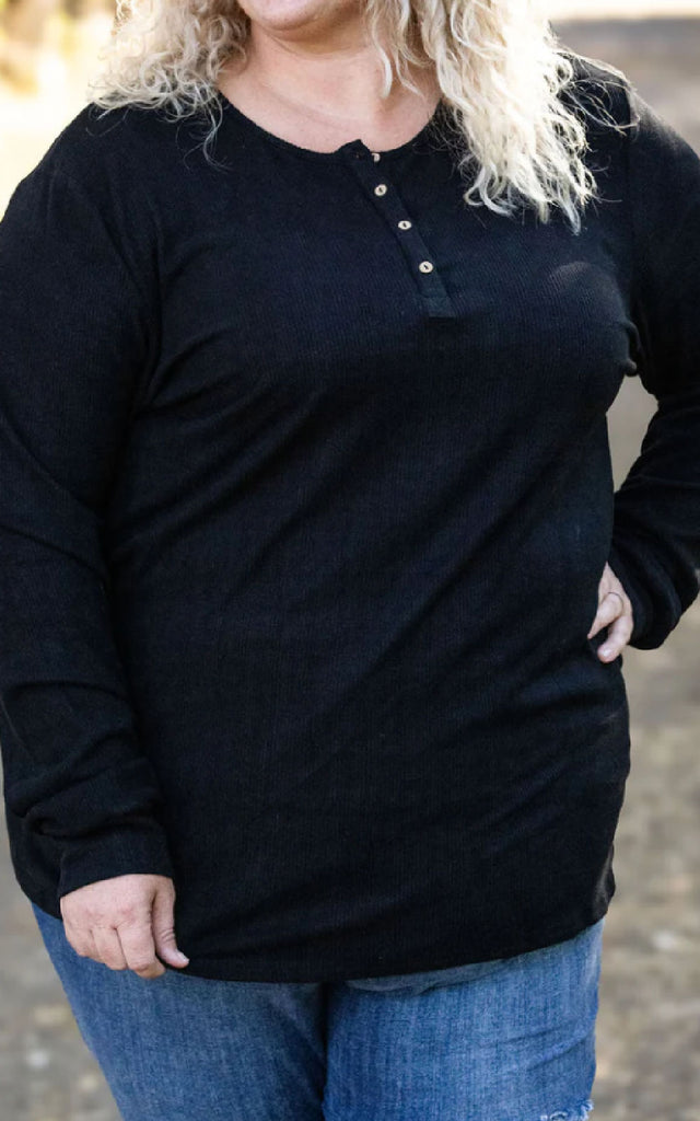 Woman posing while wearing a black henley long sleeve top.