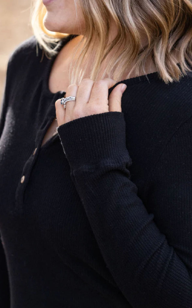 Woman posing while wearing a black henley long sleeve top.