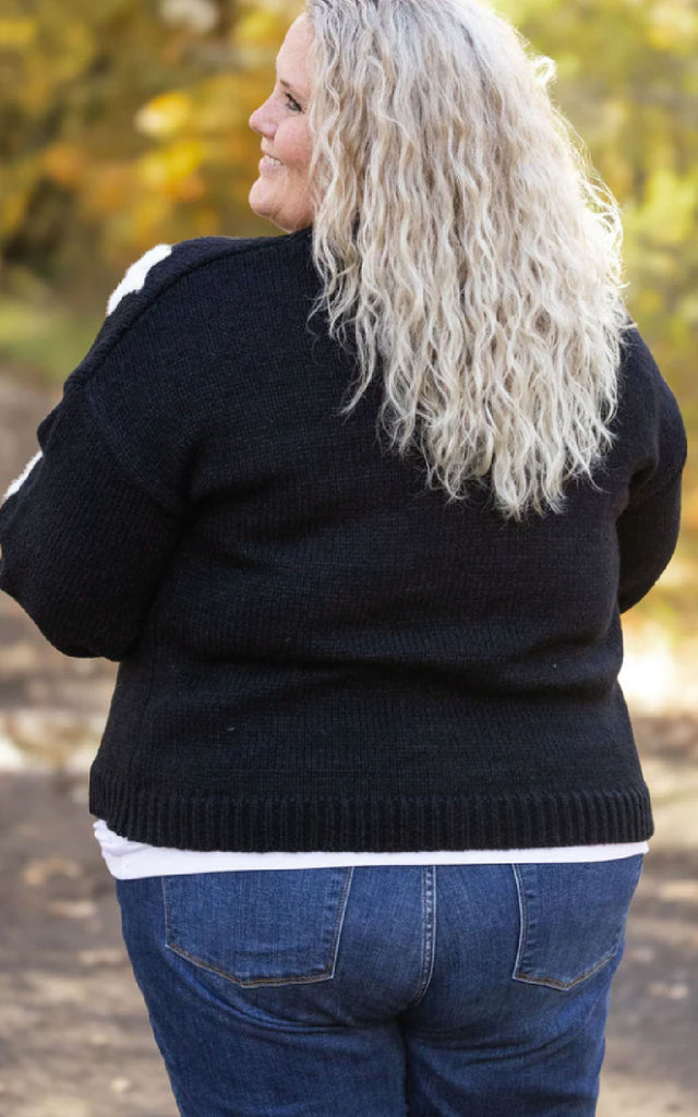 Woman wearing a whimsical holiday sweater that is black with white applique snowflakes. 