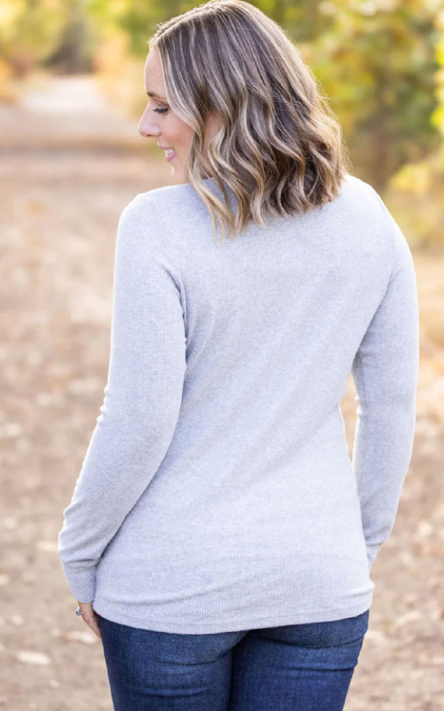 Woman posing while wearing a gray, long sleeve henley top.