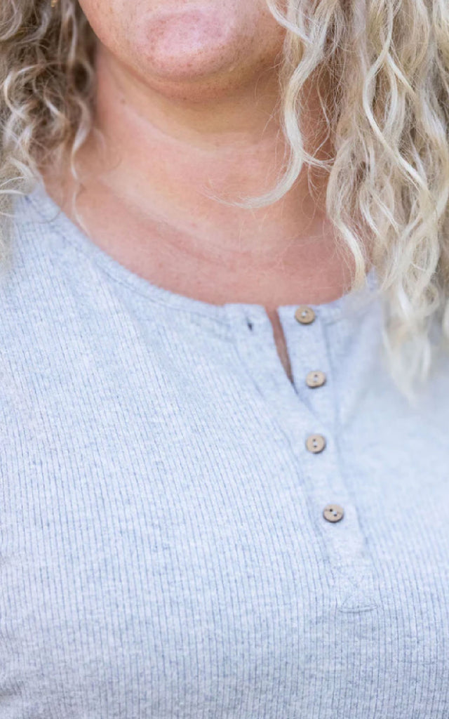 Woman posing while wearing a gray, long sleeve henley top.