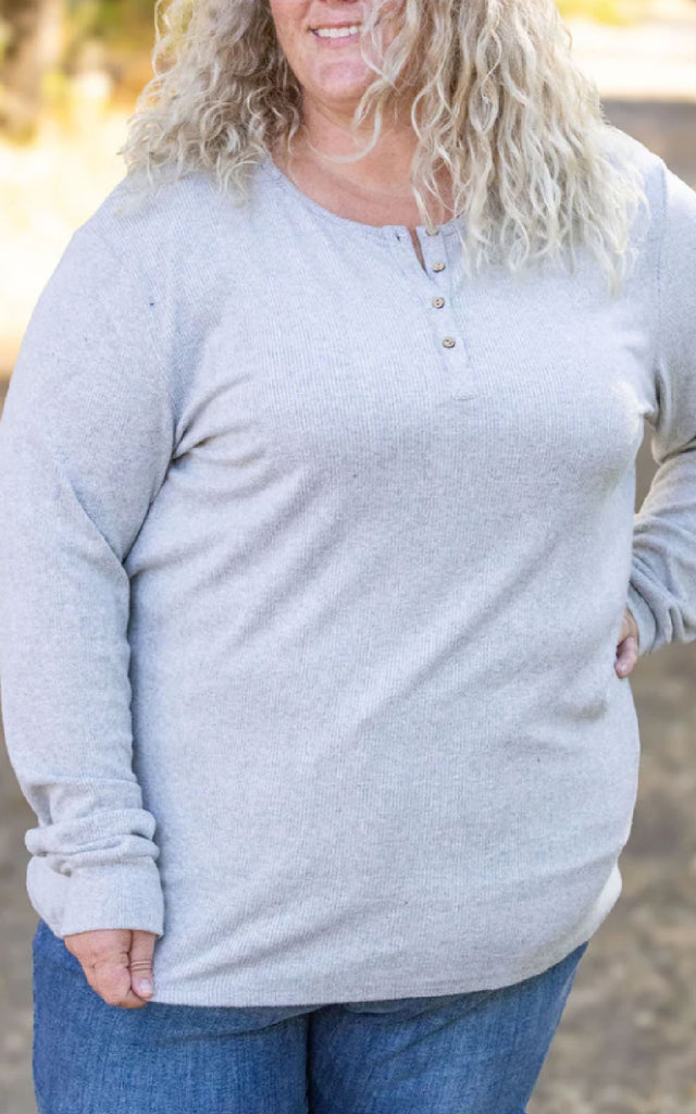 Woman posing while wearing a gray, long sleeve henley top.