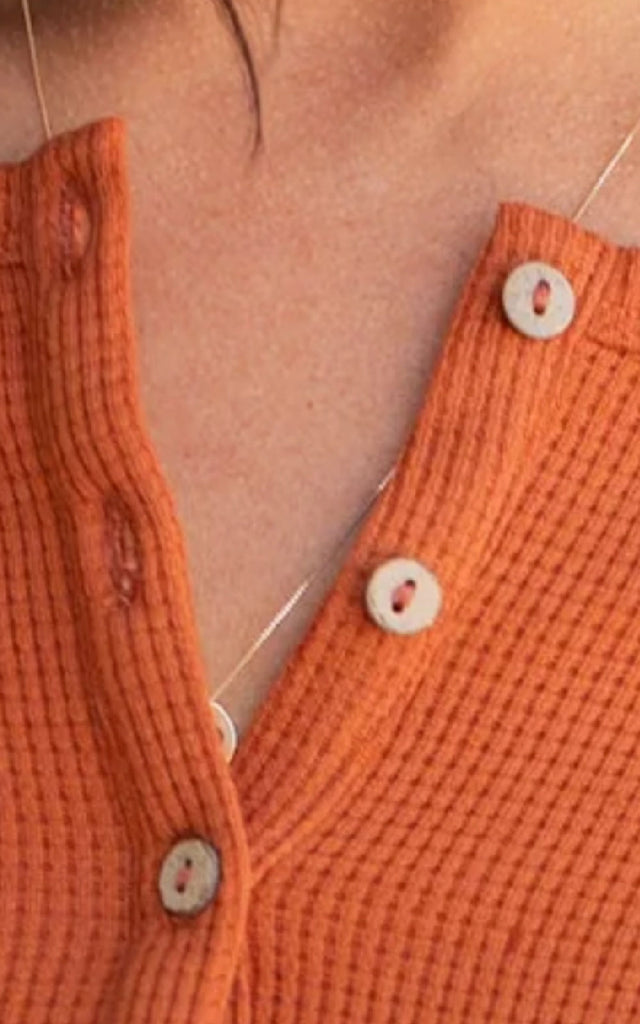 Woman wearing a long sleeve orange henley top.