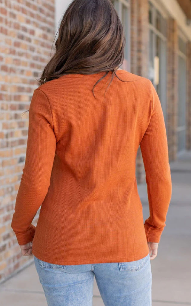 Woman wearing a long sleeve orange henley top.