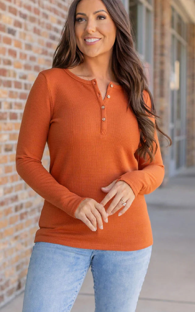 Woman wearing a long sleeve orange henley top.