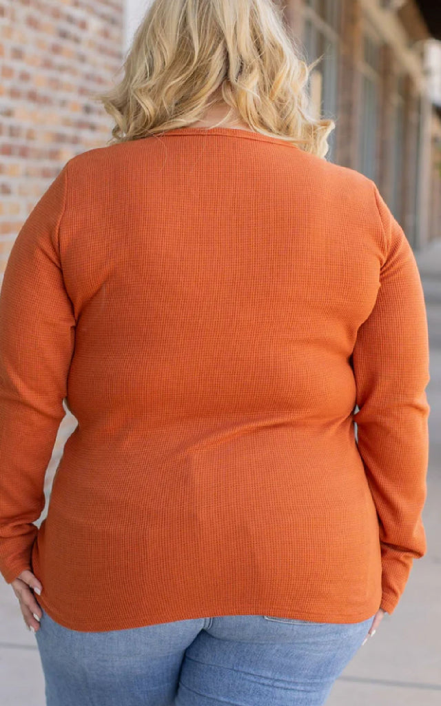 Woman wearing a long sleeve orange henley top.