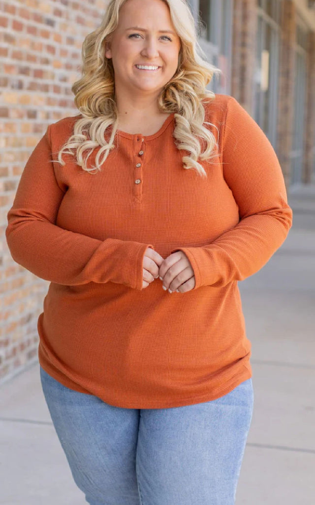 Woman wearing a long sleeve orange henley top.