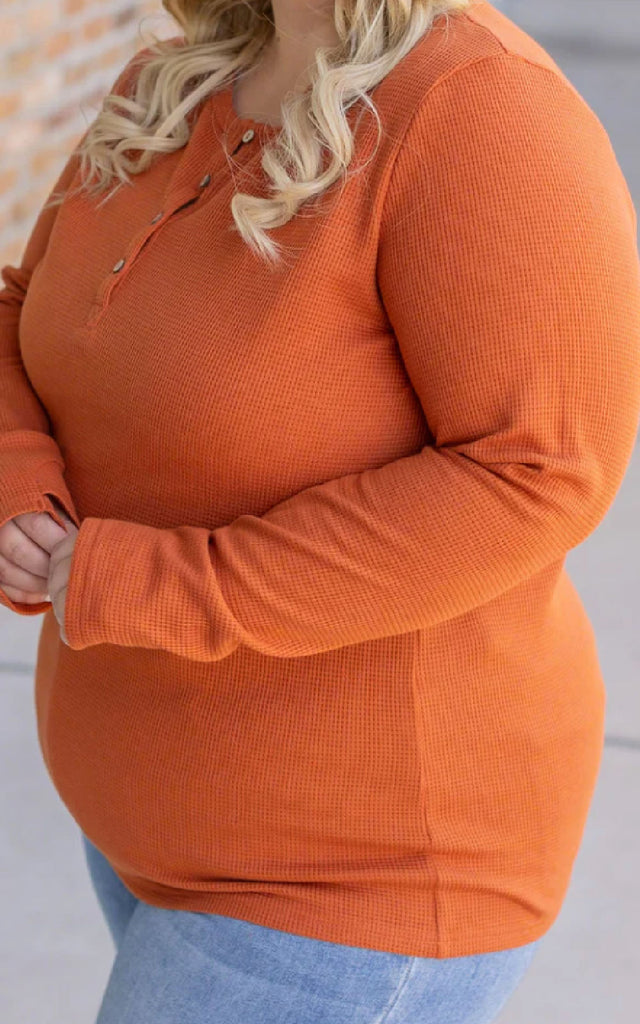 Woman wearing a long sleeve orange henley top.