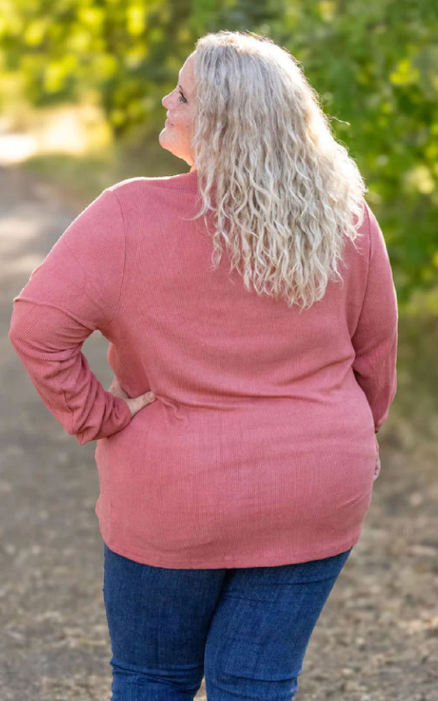 Woman posing while wearing a dark pink long sleeve henley top. 