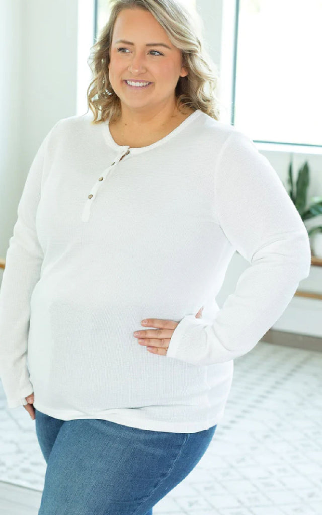 Woman wearing a white henley long sleeved shirt.