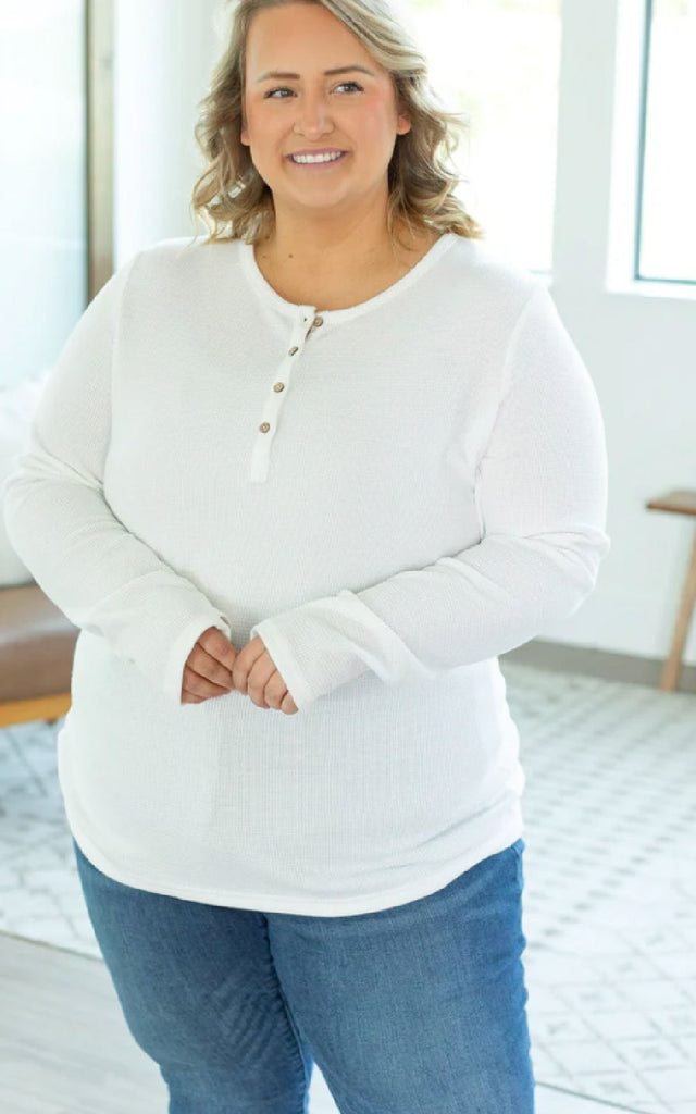 Woman wearing a white henley long sleeved shirt.